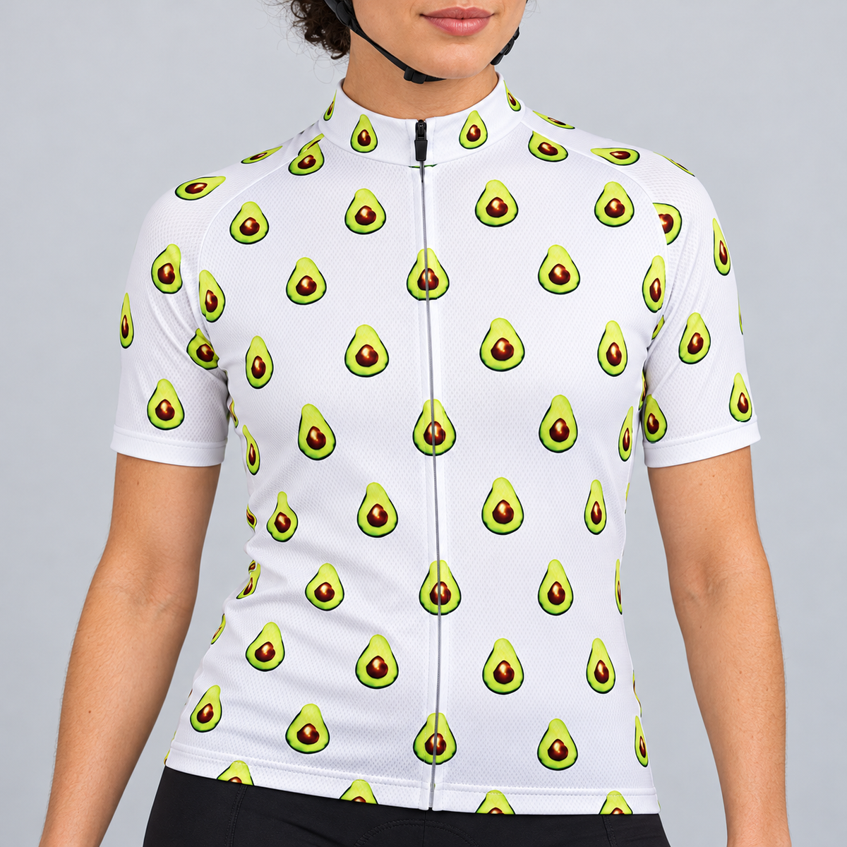 Female model wearing the white short-sleeve Avocado Pattern cycling jersey with repeating green avocado graphics and black cycling shorts, shown against a light grey studio background.