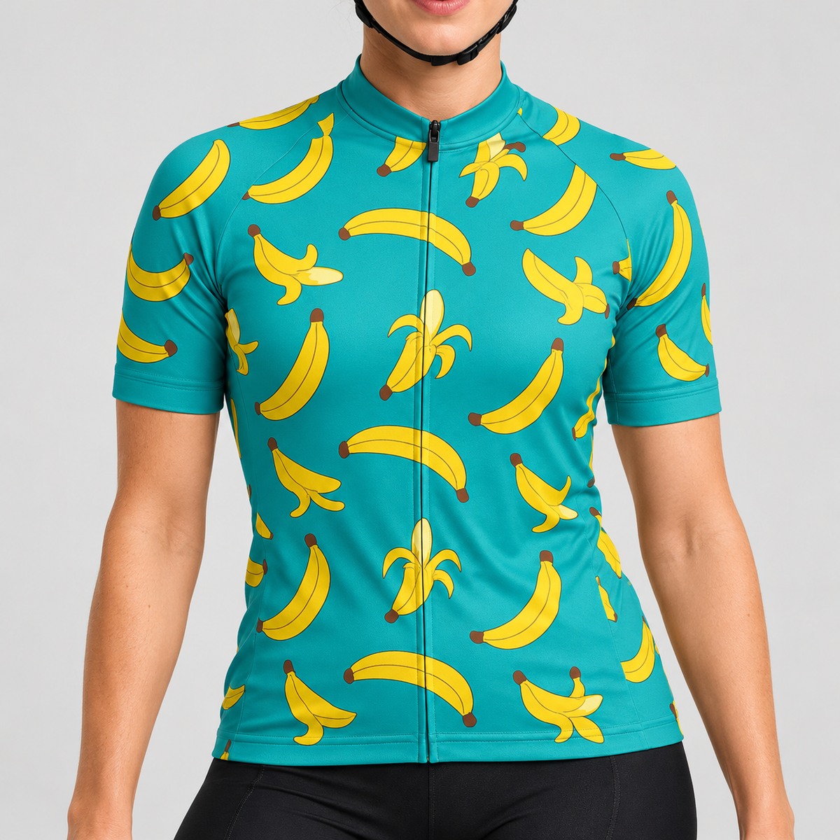 Female model wearing the turquoise short-sleeve Banana Print cycling jersey with yellow banana graphics and black cycling shorts, shown from the lower lip and chin down against a light grey studio background.