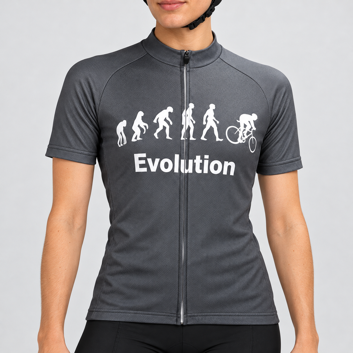 Female model wearing the charcoal-grey short-sleeve Evolution Of Man cycling jersey with white evolution silhouettes, cyclist graphic and Evolution wording, shown with black cycling shorts against a light neutral studio background.