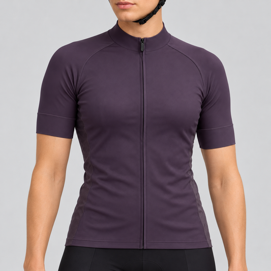 Female model wearing the plain dark purple short-sleeve GG BASICS cycling jersey with matching collar, cuffs and mesh side panels, shown with black cycling shorts against a light grey studio background.