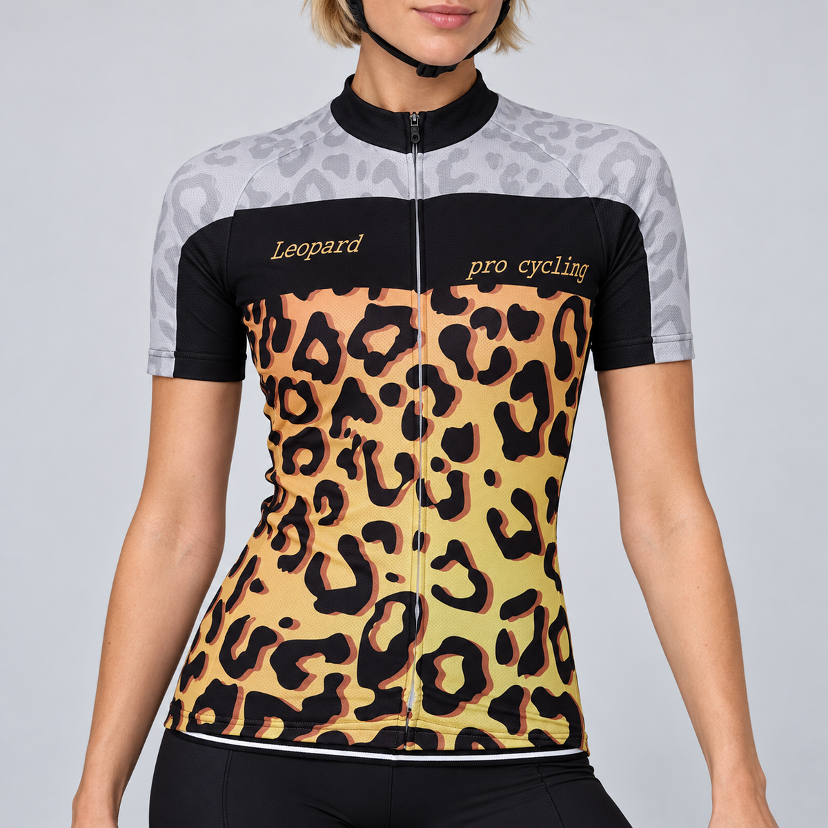 Female model wearing the short-sleeve Leopard Print cycling jersey with pale grey shoulders, black chest panel, gold and black leopard-print body, and black cycling shorts against a light grey studio background.