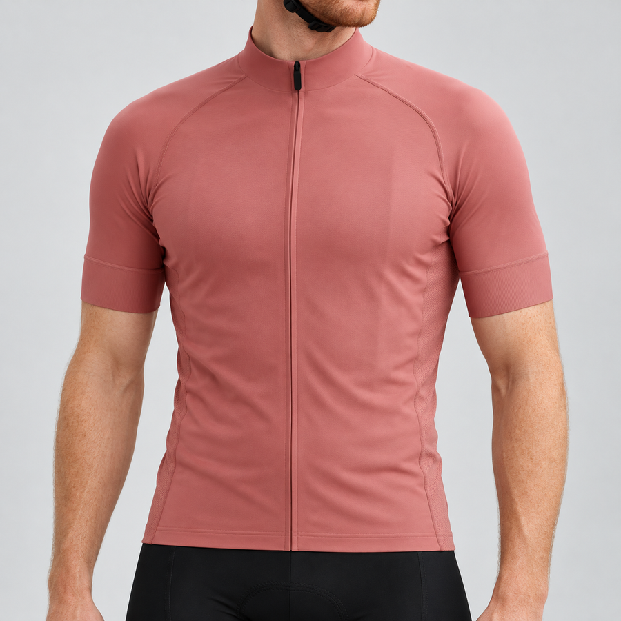 Male model wearing the plain rose-gold short-sleeve GG BASICS cycling jersey with matching collar and cuffs and mesh side panels, shown with black cycling shorts against a light grey studio background.