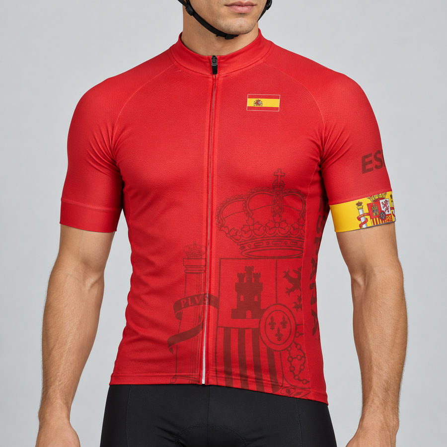 Male model shown from the chin down wearing the red Spain short-sleeve cycling jersey with Spanish flag and tonal heraldic graphics against a light grey studio background.