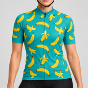 Female model wearing the turquoise short-sleeve Banana Print cycling jersey with yellow banana graphics and black cycling shorts, shown from the lower lip and chin down against a light grey studio background.