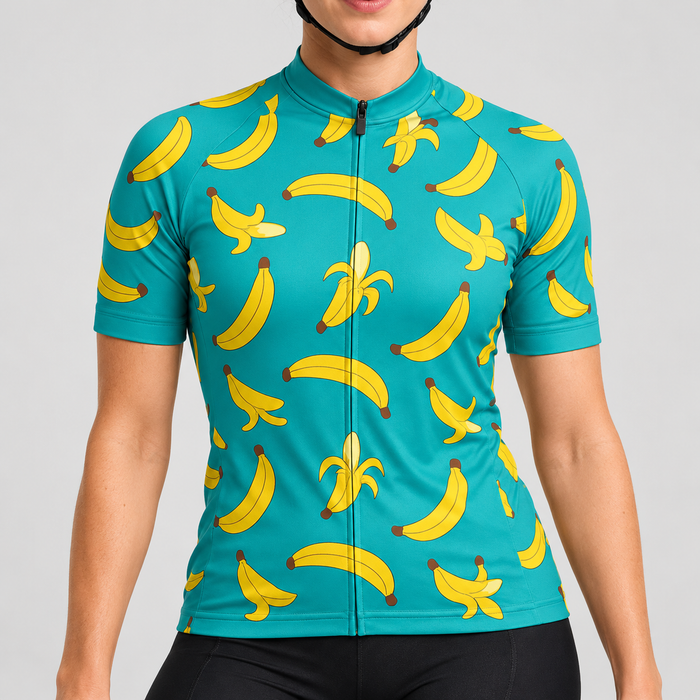 Female model wearing the turquoise short-sleeve Banana Print cycling jersey with yellow banana graphics and black cycling shorts, shown from the lower lip and chin down against a light grey studio background.
