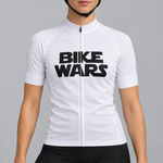 Female model wearing the white short-sleeve Bike Wars cycling jersey with bold black BIKE WARS lettering and black cycling shorts, shown from the lower lip and chin down against a light grey studio background.