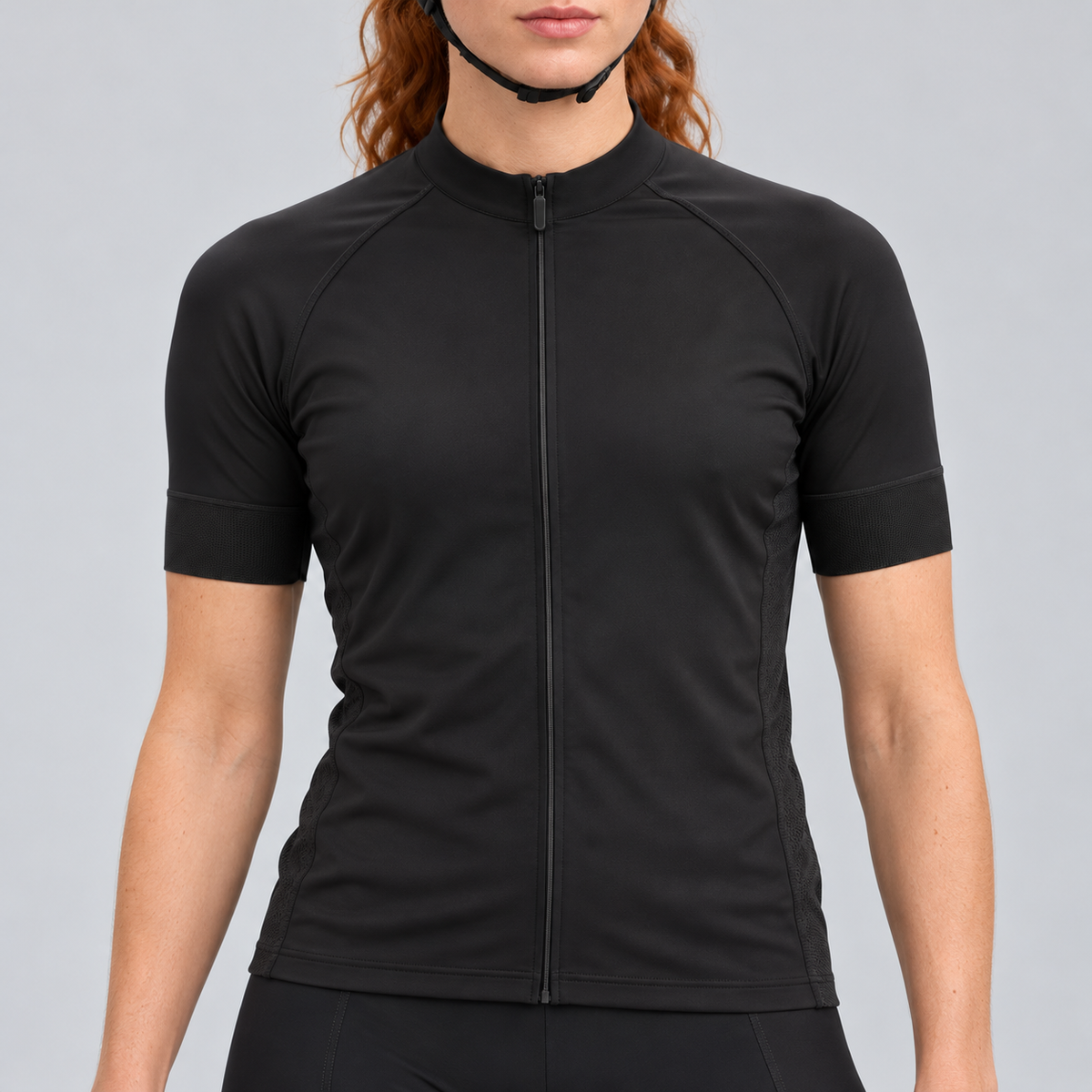 Female model wearing the plain black short-sleeve GG BASICS cycling jersey with black collar, cuffs and side panels, shown with black cycling shorts against a light grey studio background.
