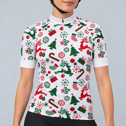 Female model wearing the white short-sleeve Christmas cycling jersey with red and green reindeer, trees, snowflakes, stockings, presents and candy canes, shown with black cycling shorts against a light grey studio background.