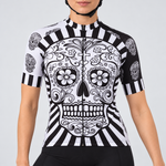Female model wearing the black-and-white short-sleeve Day Of The Dead Skull cycling jersey with a large calavera skull and radiating stripe design, shown with black cycling shorts against a light grey studio background.