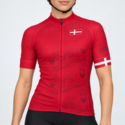 Female model wearing the red short-sleeve Denmark cycling jersey with Danish flag details, tonal crowned-lion and heart graphics, and black cycling shorts against a light neutral studio background.