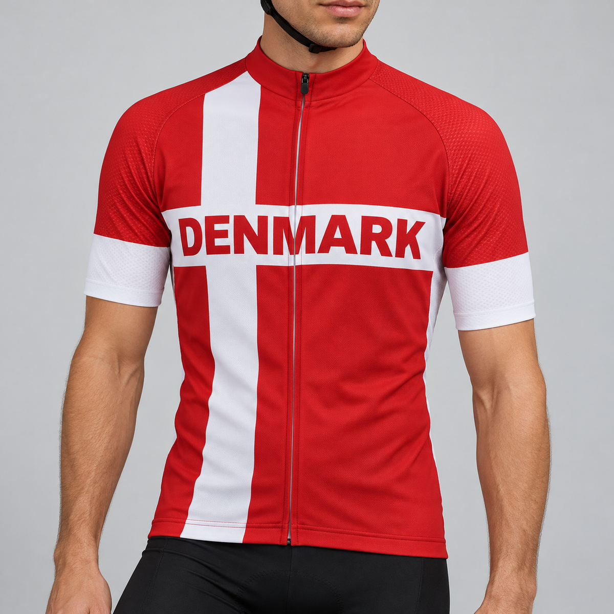 Male model wearing the red and white short-sleeve Denmark Flag cycling jersey with DENMARK lettering and black cycling shorts, shown from the chin down against a neutral studio background.
