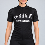 Female model wearing the black short-sleeve Evolution Of Man cycling jersey with white evolution silhouettes, cyclist graphic and Evolution wording, shown with black cycling shorts against a light neutral studio background.