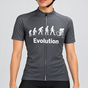 Female model wearing the charcoal-grey short-sleeve Evolution Of Man cycling jersey with white evolution silhouettes, cyclist graphic and Evolution wording, shown with black cycling shorts against a light neutral studio background.