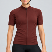 Female model wearing the plain burgundy short-sleeve GG BASICS cycling jersey with matching collar, cuffs and mesh side panels, shown with black cycling shorts against a light grey studio background.