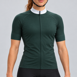Female model wearing the dark green short-sleeve GG BASICS cycling jersey with a white collar, matching green cuffs and mesh side panels, shown with black cycling shorts against a light grey studio background.