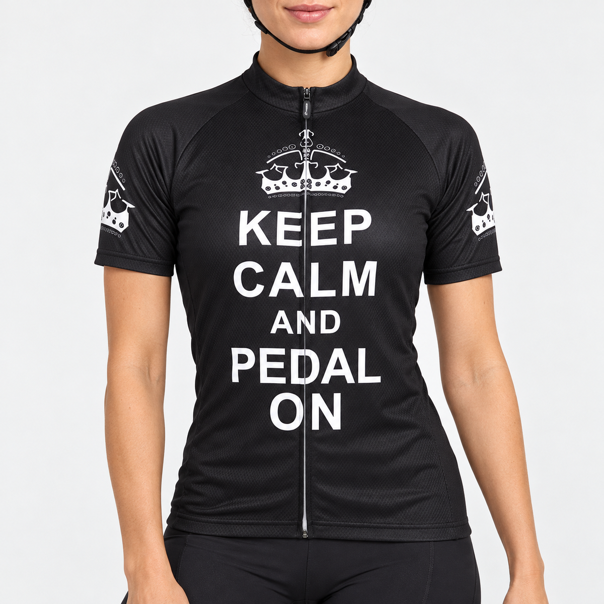Female model wearing the black short-sleeve Keep Calm and Pedal On cycling jersey with white crown graphics and stacked white lettering, shown with black cycling shorts against a light grey studio background.