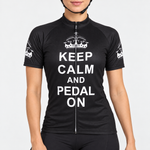 Female model wearing the black short-sleeve Keep Calm and Pedal On cycling jersey with white crown graphics and stacked white lettering, shown with black cycling shorts against a light grey studio background.