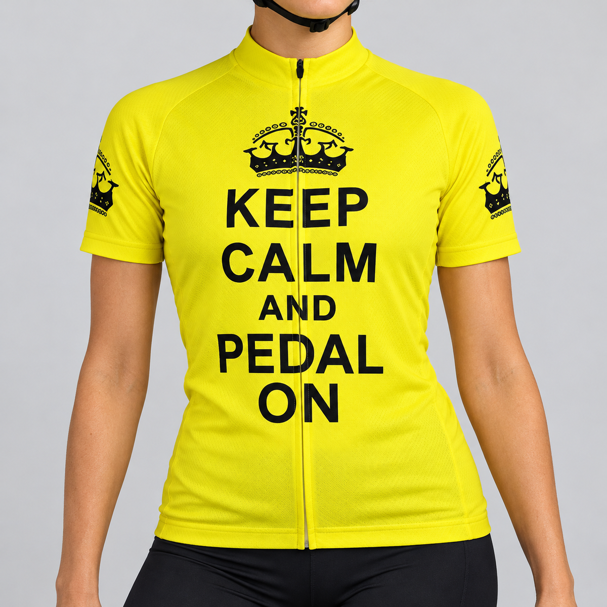 Female model wearing the bright yellow short-sleeve Keep Calm and Pedal On cycling jersey with black crown graphics and stacked black lettering, shown from the chin down with black cycling shorts against a light grey studio background.
