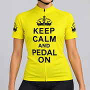 Female model wearing the bright yellow short-sleeve Keep Calm and Pedal On cycling jersey with black crown graphics and stacked black lettering, shown from the chin down with black cycling shorts against a light grey studio background.