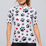 Female model wearing the white short-sleeve Paws & Love cycling jersey with black paw-print and red-heart graphics and black cycling shorts against a light grey studio background.