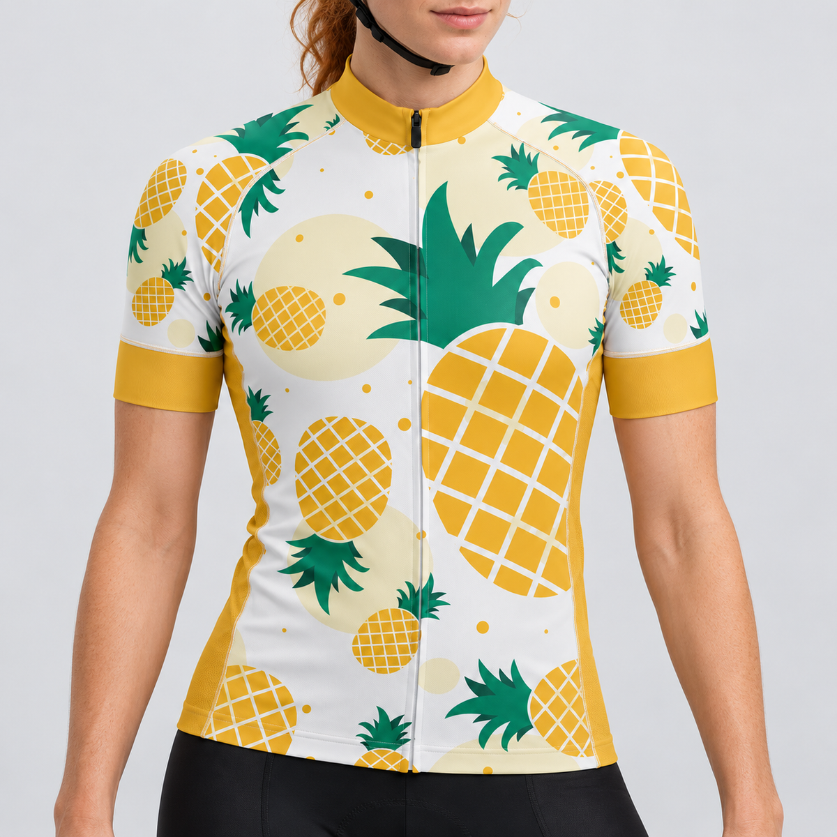 Female model wearing the ivory, mustard yellow and green short-sleeve Pineapple Print cycling jersey with black cycling shorts against a light grey studio background.