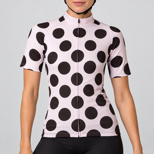 Female model wearing the pale pink short-sleeve cycling jersey with large black polka dots and black cycling shorts against a light grey studio background.