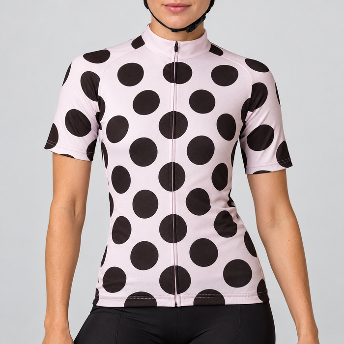 Female model wearing the pale pink short-sleeve cycling jersey with large black polka dots and black cycling shorts against a light grey studio background.