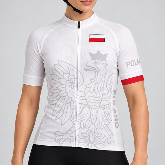Female model wearing the white short-sleeve Poland cycling jersey with a pale-grey crowned eagle, Polish flag badge and red sleeve trim, shown with black cycling shorts against a light grey studio background.