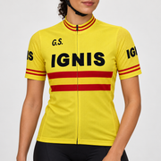 Female model wearing the yellow short-sleeve Retro Ignis cycling jersey with black G.S. and IGNIS lettering, red torso and cuff stripes, and black cycling shorts against a light grey studio background.