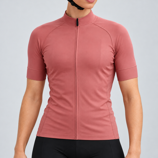 Female model wearing the plain rose-gold short-sleeve GG BASICS cycling jersey with matching collar, cuffs and mesh side panels, shown with black cycling shorts against a light grey studio background.