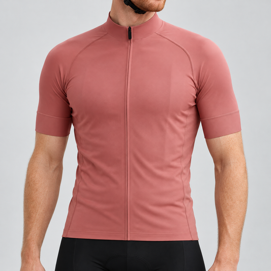 Male model wearing the plain rose-gold short-sleeve GG BASICS cycling jersey with matching collar and cuffs and mesh side panels, shown with black cycling shorts against a light grey studio background.