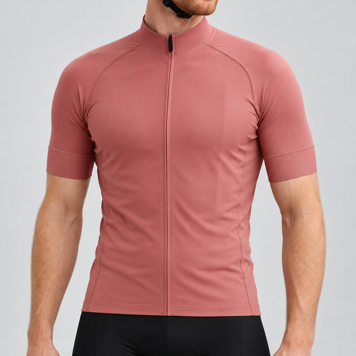 Male model wearing the plain rose-gold short-sleeve GG BASICS cycling jersey with matching collar and cuffs and mesh side panels, shown with black cycling shorts against a light grey studio background.